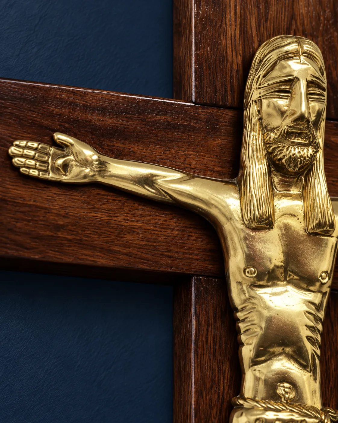 Detalle del brazo derecho extendido y el rostro de Cristo, sobre la cruz de madera